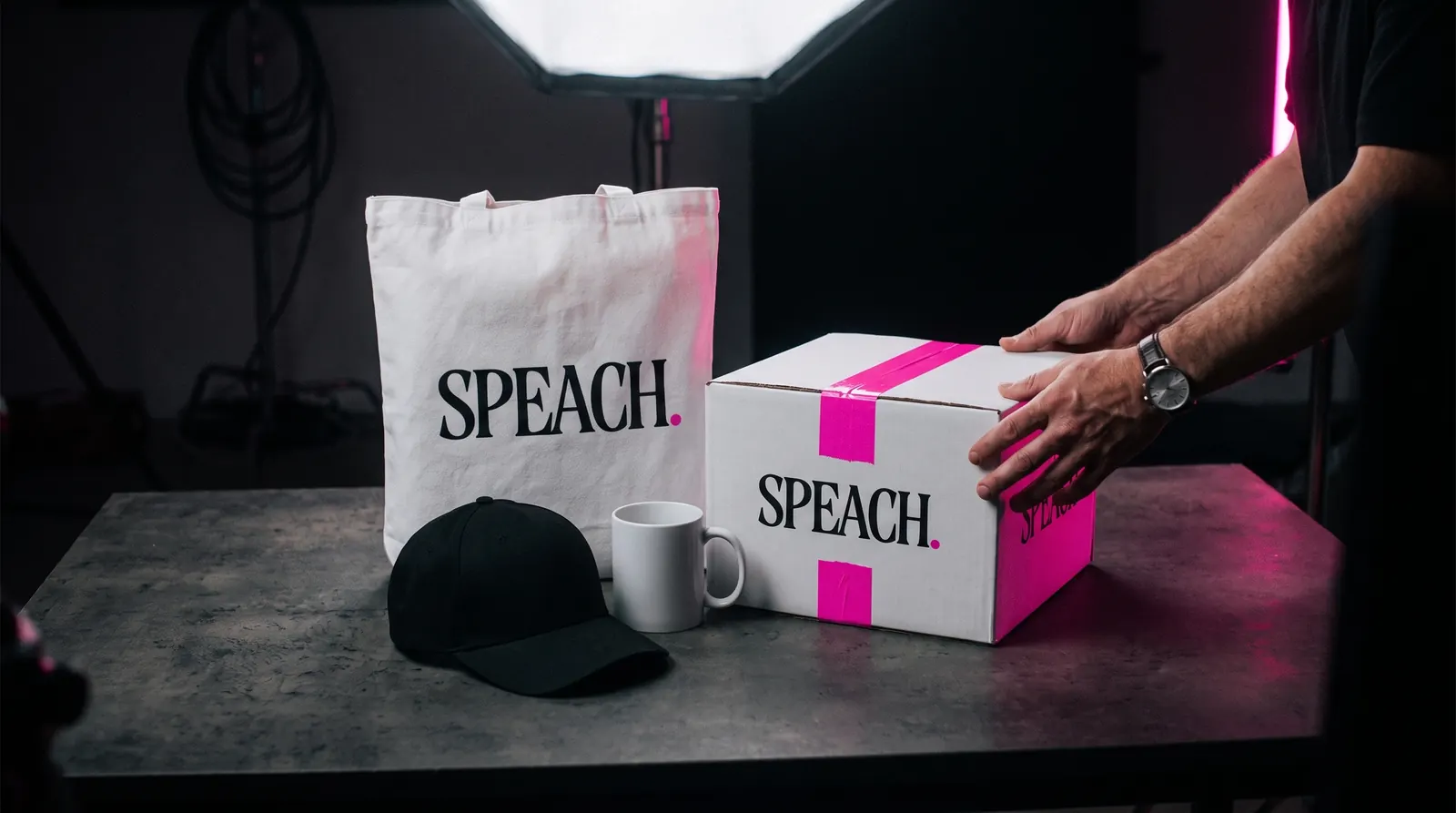 Mercancía de SPEACH en el set: bolsa de tela y caja sellada con cinta rosa con el logotipo