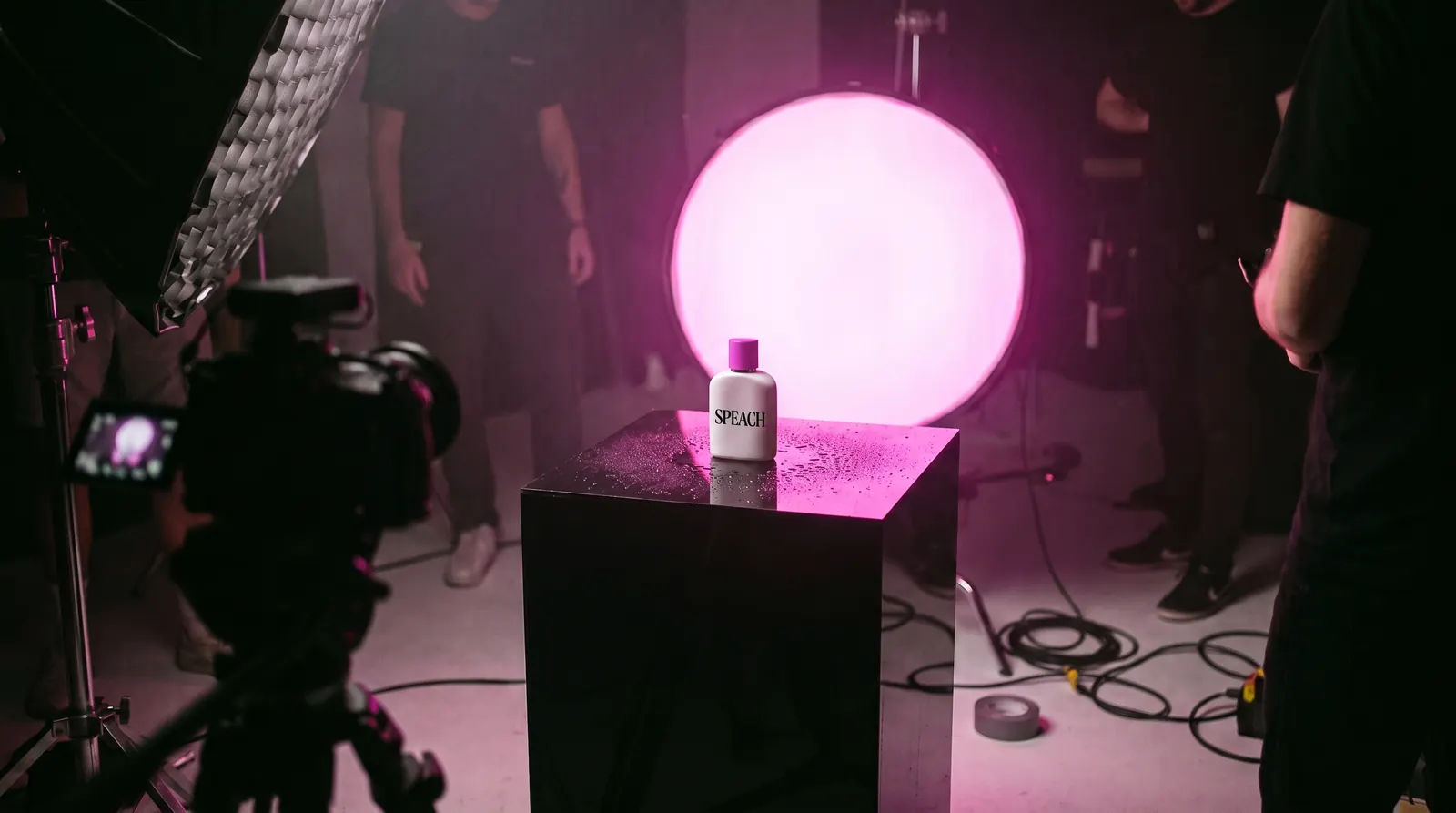 Set de fotografía de producto: un frasco blanco con etiqueta de SPEACH sobre acrílico negro, frente a un disco de luz rosa